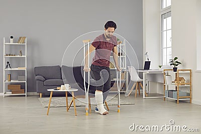 Man with broken leg stands up from chair and starts walking with crutches at home Stock Photo