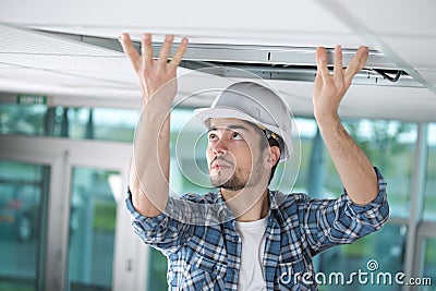 Man in builder uniform hand up installing suspended ceiling Stock Photo