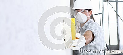 Man builder using a sponge on wall professional construction worker with mask, safety hard hat, gloves and protective glasses. Stock Photo