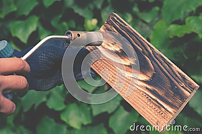 A man burns boards with fire from a gas burner Stock Photo