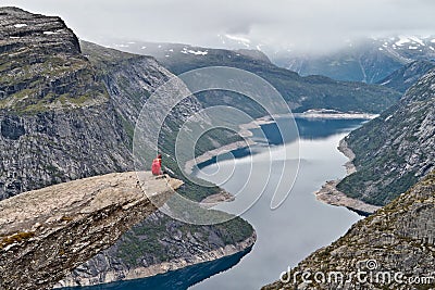 Man with camera sitting on Trolltunga rock Troll`s Tongue rock Stock Photo