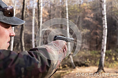 A man in camouflage clothes aims from a gas pistol in his hands in the forest in autumn Stock Photo
