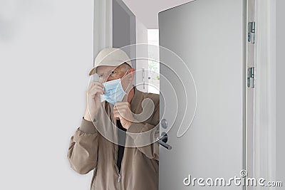 Man with cap ajusting his protective Coronavirus mask as he leaves home. Stock Photo