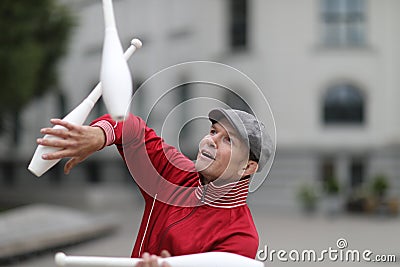 A man in a cap juggles with clubs Stock Photo