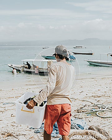 Man carrying something in a plastic container in the beach in Bali, Indonesia Editorial Stock Photo