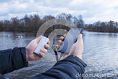 A man charges a smartphone with a power bank. The phone in hand is being charged with a portable charger against the backdrop of Stock Photo
