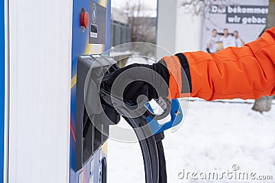 man charging electric car, holding DC charging connector in hand, ev Combined Charging System CCS2 quick-charge station, Editorial Stock Photo