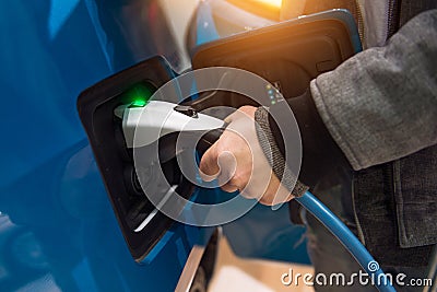 Man charging electro car at charging station. Man holding in hand power cable supply plugged in Stock Photo