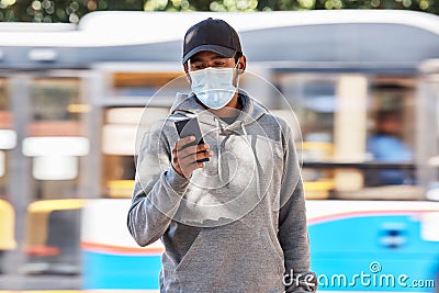 Man in city with mask, phone and travel in morning at bus stop, checking service schedule or social media. Public Stock Photo