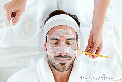 Man with clay facial mask in beauty spa. Stock Photo