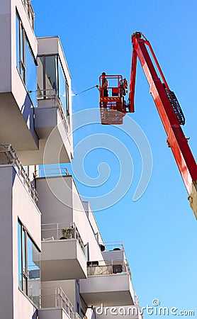 Man cleaning facade of a modern minimalistic apartment building on a telescopic boom lift using pressure jet wash with blue sky Editorial Stock Photo