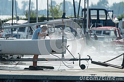 Man cleans catamaran with high-pressure sprayer in september sun Editorial Stock Photo