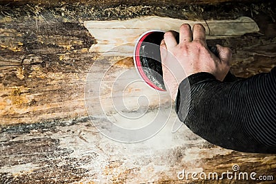A man cleans the skins of a log with a grinding machine in a wooden house Stock Photo