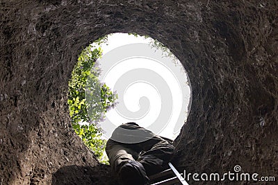 A man climbs the ladder out of the deep hole. Stock Photo