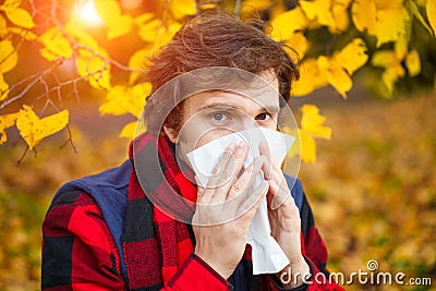 Man with cold rhinitis on autumn background. Fall flu season. Il Stock Photo