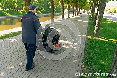 A man collects garbage in bags on the sidewalk. The concept of cleaning the city park Editorial Stock Photo