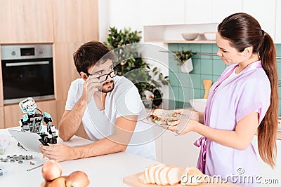 A man collects a robot in the kitchen. The girl brought him a sandwich. He looks at her with his glasses down. Stock Photo