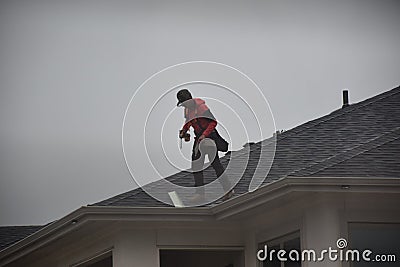 A man contractor worker on roof top working on a cloudy rainy day.standing sitting walking kneeling. fixing roof.rain water system Editorial Stock Photo