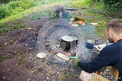 A man cooks on a fire, a tourist heats water in a pot on a fire Editorial Stock Photo