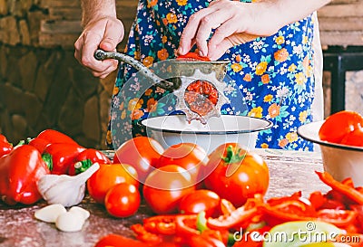 Man cooks homemade sauce, ketchup grinds pieces of ripe tomatoes into an old vintage hand meat grinder Stock Photo