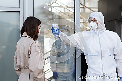 Man in coronavirus hazmat measuring temperature of a woman Stock Photo