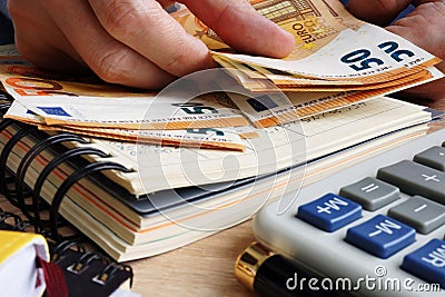 Man counting euro banknotes. Desk with calculator, ledger and euros. Stock Photo