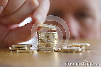 Man counts his coins on a table. Close-up of hand putting a coin to stack of gold coins. Stock Photo