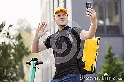 Man courier food delivery with yellow thermal backpack walks street with electric scooter Stock Photo