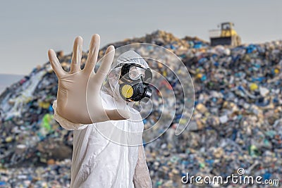 Man in coveralls is showing stop gesture. Garbage pile in landfill in background Stock Photo