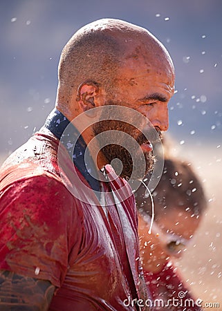 Man covered with mud splatters and dripping water while washing off after a mud run Stock Photo