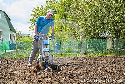 Man cultivates the soil in the garden using a motor cultivator - tiller Stock Photo