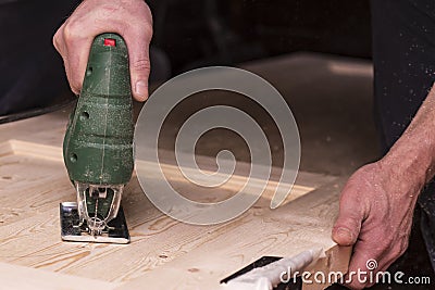 Man cuts a circle in a wooden door using an electric jigsaw joinery Stock Photo