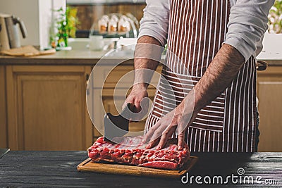 Man cuts of fresh piece of beef on a wooden cutting board in the home kitchen Stock Photo