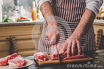 Man cuts of fresh piece of beef on a wooden cutting board in the home kitchen Stock Photo