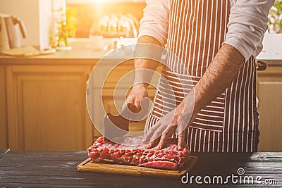 Man cuts of fresh piece of beef on a wooden cutting board in the home kitchen Stock Photo