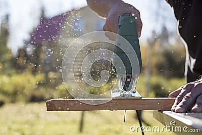 Man cuts wood product using an electric jigsaw joinery in the sun on a warm summer day. Stock Photo