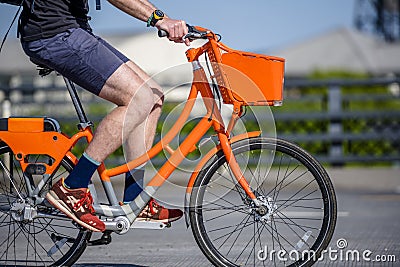 Male cyclist rides socially rented orange bicycle with basket on crossroad on city street Editorial Stock Photo