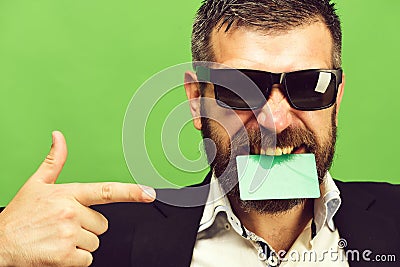Man with dark beard holds green business card in teeth Stock Photo