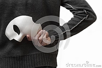 A man in dark clothing on a white background holds a white mask behind his back Stock Photo