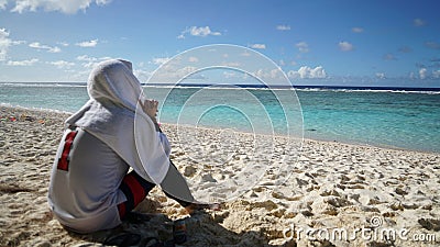 A man with a deep-thinking head and a towel over his head looking at the blue sea Stock Photo