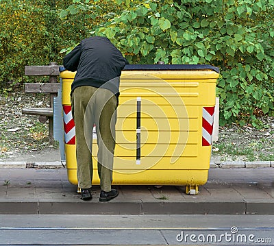 Man digging through garbage in yellow recycling container Stock Photo