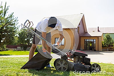 Man disconnects a full grass catcher on a lawn mower. Stock Photo