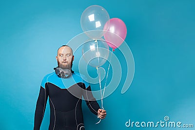 Man in diver suit making funny face and holding birthday balloons against blue studio wall banner background Stock Photo