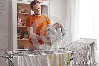 Man doing home chores. Caucasian man removes clothing and baby sheets after laundry from portable dryer in living room Stock Photo