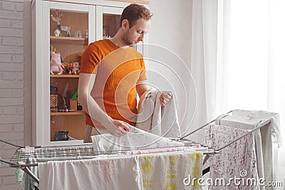 Man doing home chores. Caucasian man removes clothing and baby sheets after laundry from portable dryer in living room Stock Photo