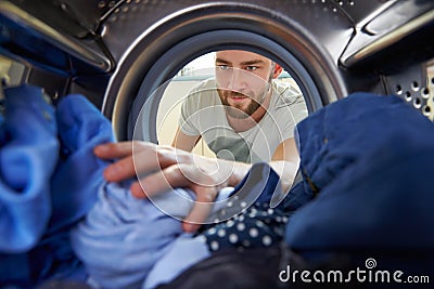 Man Doing Laundry Reaching Inside Washing Machine Stock Photo