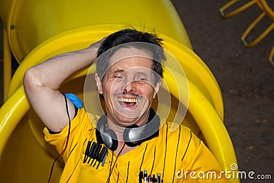 Man With Downs Syndrome Laughs and Plays on a Playground Slide Stock Photo