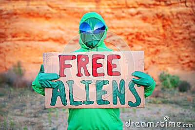 A man dressed in a green alien carnival costume suit at a lone rally with a sign `free aliens` on the background of a desert can Stock Photo