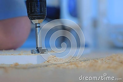 Man drilling round hole in chipboard wardrobe door for hinges making furniture. Stock Photo