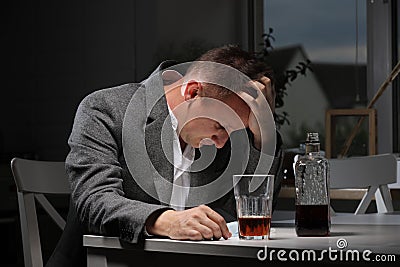 man drinking alcohol in the kitchen after work. Young man suffering from strong headache or migraine sitting with glass Stock Photo